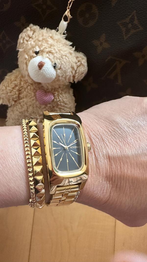 Woman showing off her gold Frankie analog watch with a teddy bear in the background