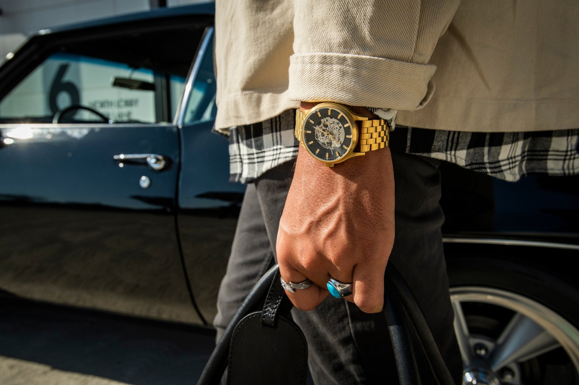 Man carrying a bag and wearing the gold Nixon Spectra dress watch