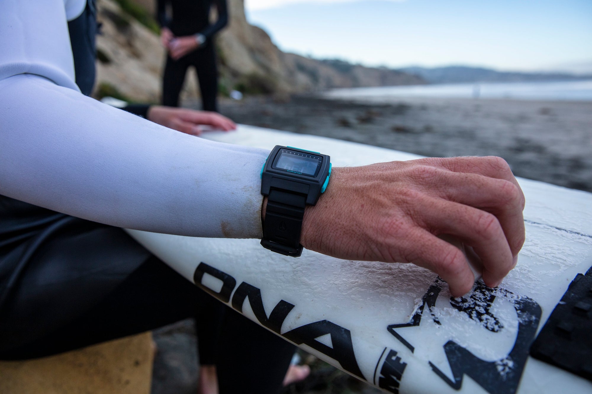 Surfer waxes his surf board while wearing a Nixon Base Tide Pro watch.