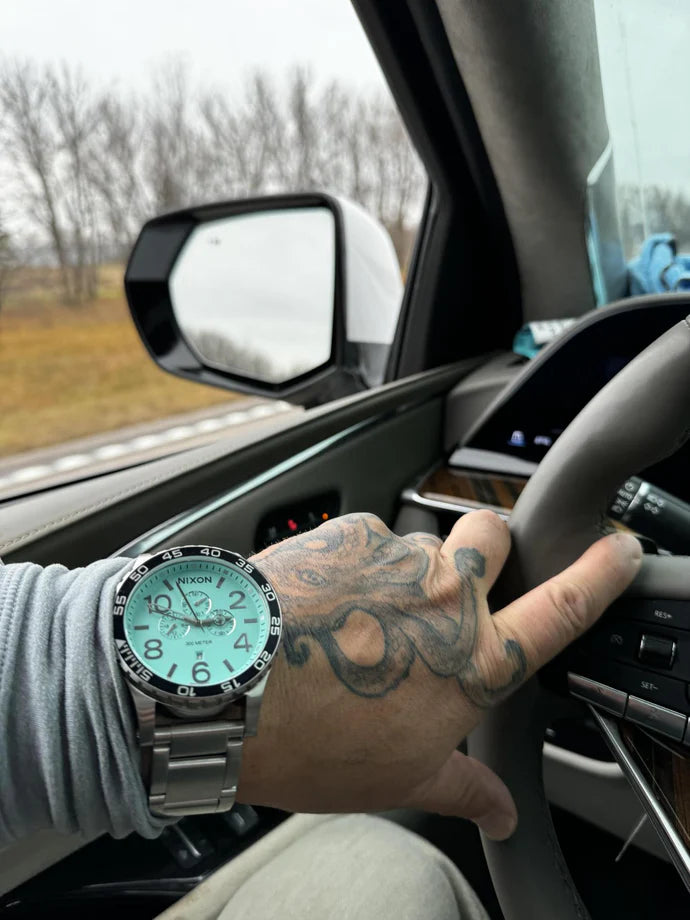 Man driving his car and showing off his turquoise blue Nixon 51-30 Chrono watch.