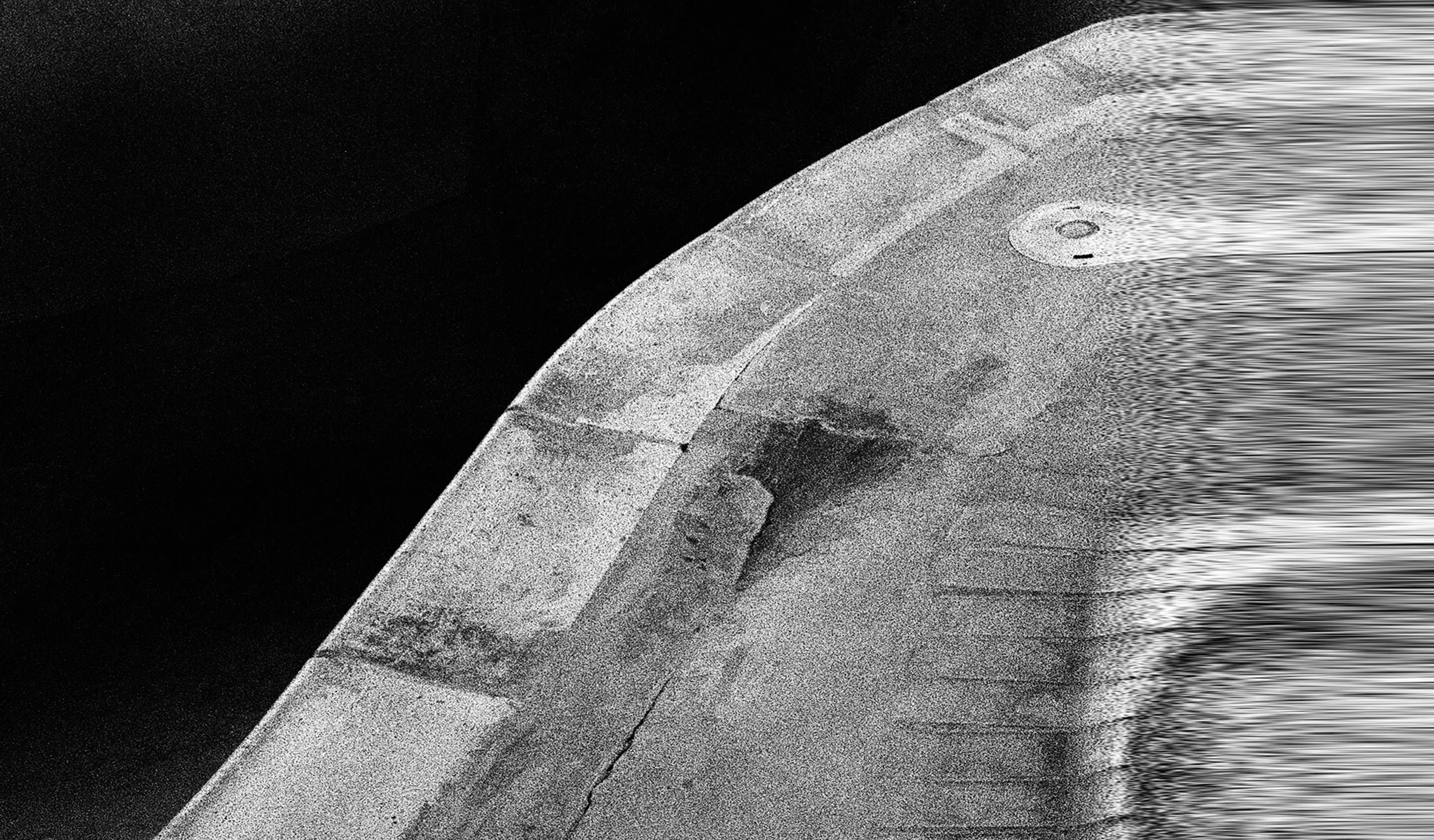 Abstract black and white image featuring a curved, grainy concrete-like structure on the right with horizontal lines and a small circular detail, set against a dark background, suitable for a website footer.