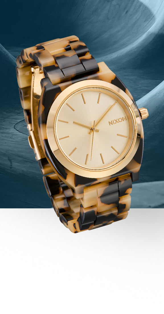 A Nixon wristwatch with a gold-tone case and dial, paired with a brown and black tortoiseshell-patterned link bracelet, shown against a split blue and white background.