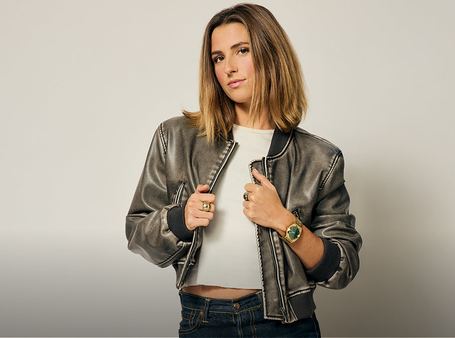 Woman wearing a metallic jacket against a plain background wearing a Nixon watch