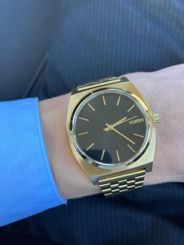 Man wearing a gold Nixon Time Teller analog watch with a blue suit